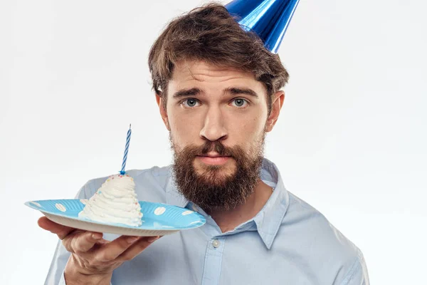 Un hombre con un plato de pastel y una camisa azul sobre un fondo claro fiesta de cumpleaños gorra corporativa — Foto de Stock