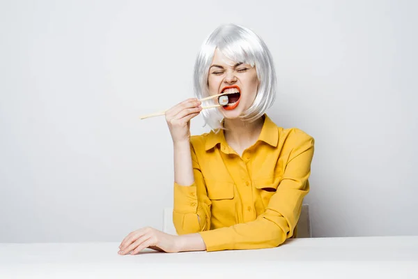 Χαρούμενη ξανθιά με ξυλάκια σούσι να τρώει καθισμένη στο τραπέζι — Φωτογραφία Αρχείου
