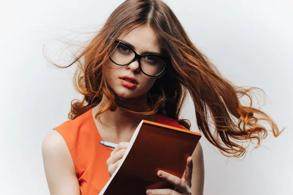 Woman in an orange sundress on a light background with a notebook and a pen in her hand a student of education — Stock Photo, Image