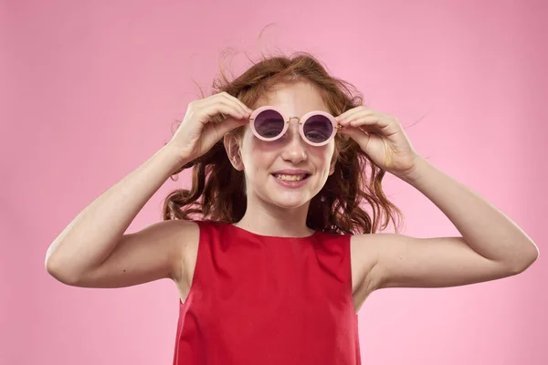 Χαρούμενο κοριτσάκι παιδική ηλικία σκούρα γυαλιά κόκκινο φόρεμα lifestyle ροζ φόντο — Φωτογραφία Αρχείου