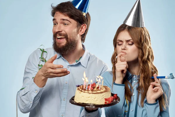 Homem de aniversário mulher em chapéus de festa em um fundo azul e bolo com velas — Fotografia de Stock