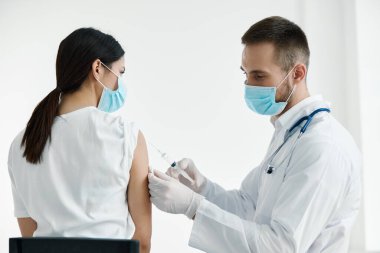Beyaz önlüklü doktor bir kadına omuz aşısı koruyucu eldiven enjekte ediyor.