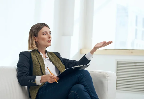 Frau gestikuliert mit den Händen und sitzt drinnen am Fenster auf dem Sofa — Stockfoto