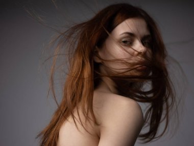Gri arka planda kızıl saçlı güzel bir kadın çıplak omuzlarını yakın plan manken gibi gösteriyordu.