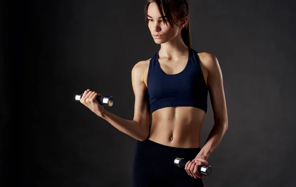 Mujer con músculos haciendo mancuernas deportivas en sus manos y figura delgada — Foto de Stock