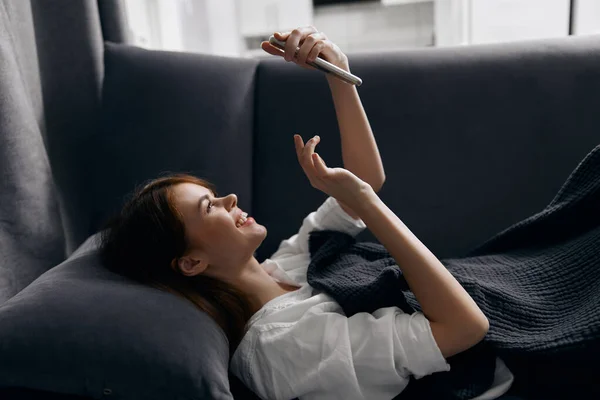 happy woman looking at phone screen while lying on sofa indoors