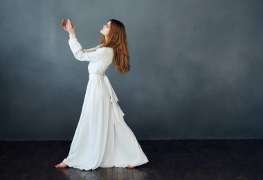 Beyaz elbiseli güzel bir kadın, gri bir arka planda, tamamen büyümüş bir şekilde yere uzanıyor.