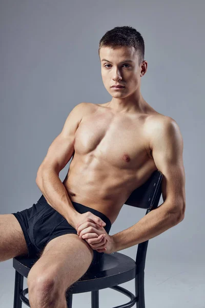 Athletic guy with a pumped-up body in black panties sits on a chair — Stock Photo, Image