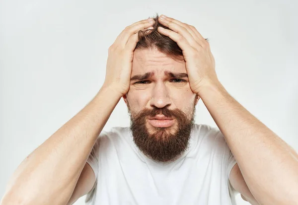 Emotionele man in een T-shirt raakt zijn hoofd met zijn handen op een lichte achtergrond bijgesneden uitzicht — Stockfoto