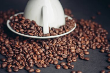 Kahve tanecikleri ters dönmüş kupa ve çay tabağı gri Arabika masasında.