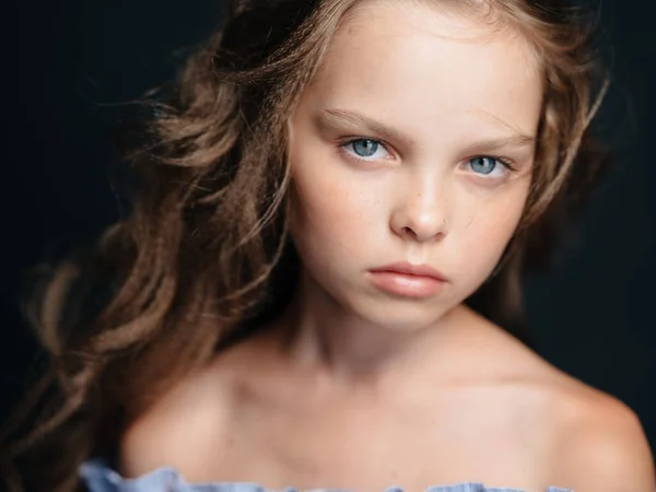 Egy gyönyörű kék szemű lány, csupasz vállakkal, sötét háttérrel és göndör hajjal. — Stock Fotó