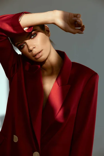 Mulher bonita com maquiagem brilhante segura a mão acima de sua cabeça sombreando a luz jaqueta vermelha — Fotografia de Stock