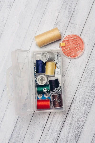 Skein of multicolored thread in a plastic box wooden background needles safety pin sewing supplies — Stock Photo, Image