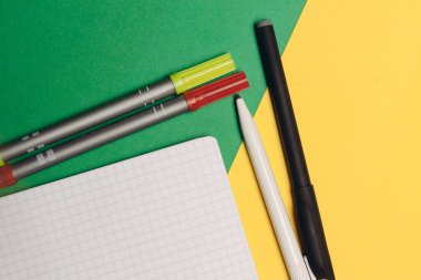 Parlak arkaplanda renkli kalemler ve işaretler ve masada beyaz bir not defteri.