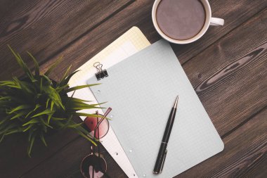 Ahşap bir masa üzerinde defter ve kalem. Kahve fincanı çiçeği, tencere manzaralı.