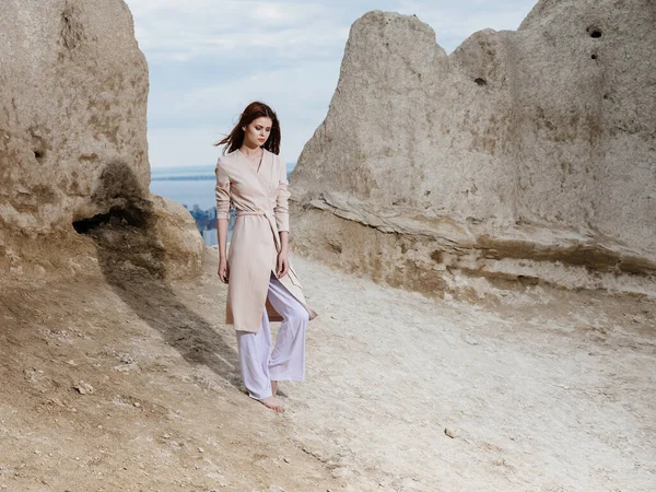 Romantische reiziger in lichte kleren op het zand in de buurt van hoge rotsen — Stockfoto