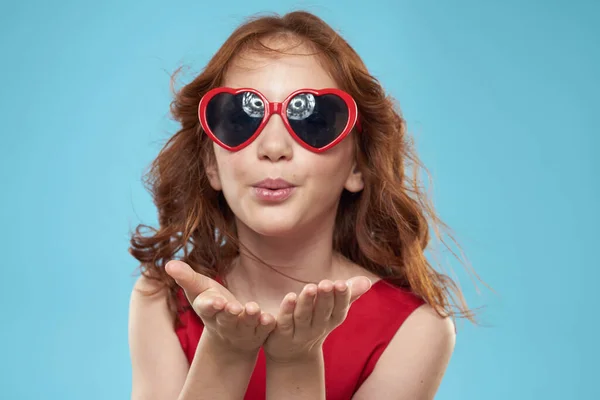 Chica con gafas de sol de pelo rizado vestido rojo y la infancia divertido fondo azul — Foto de Stock