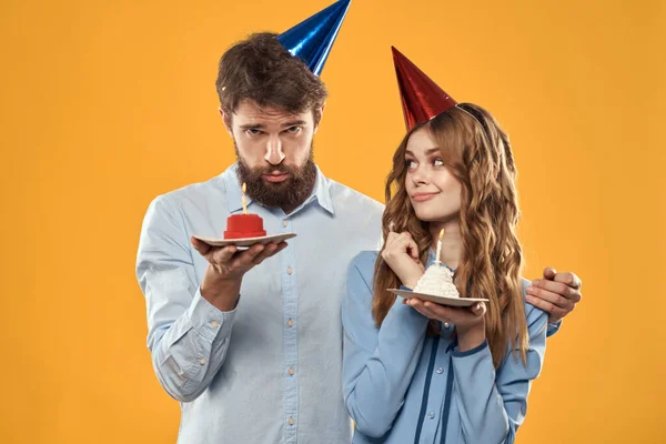 Muž a žena s narozeninovým dortem a v čepicích na žlutém pozadí party zábava žluté pozadí — Stock fotografie