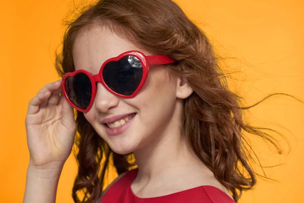 Ragazza in occhiali neri vestito rosso infanzia divertimento giallo sfondo — Foto Stock