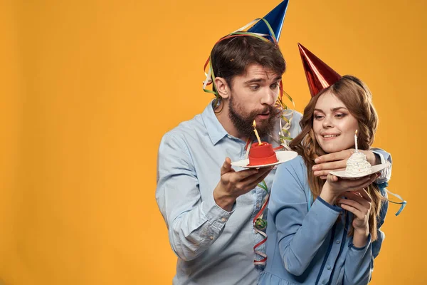 Muž a žena na party v čepicích a s tinsel dort zábava žluté pozadí — Stock fotografie