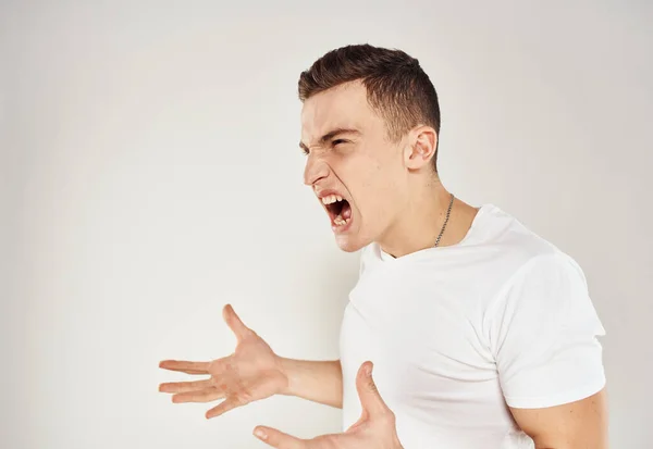 Een man in een wit T-shirt emoties prikkelbaarheid licht achtergrond onvoldoende staat — Stockfoto
