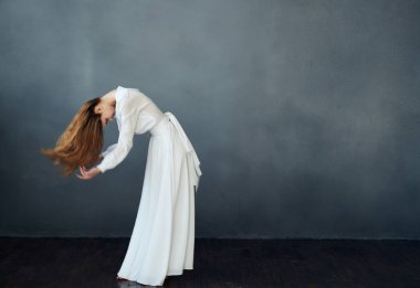 Beyaz elbiseli bir kadın gri arka planda kızıl saçlı bir modelle dans ediyor.