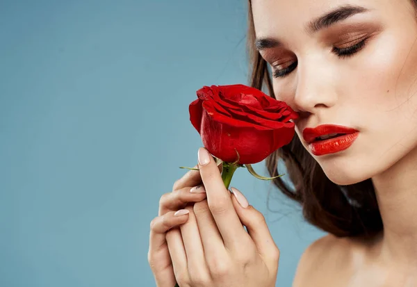 Una donna tiene in mano un fiore rosso su sfondo blu e trucco sul viso — Foto Stock