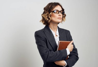 Klasik takım elbiseli bir iş kadını, elinde bir kitapla evin içinde hafif bir arka plan tutuyor.