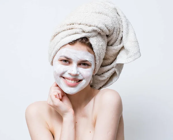 Una mujer cuida de su apariencia y una toalla en su cabeza y una crema hidratante en su cara —  Fotos de Stock