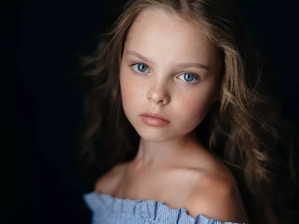 Beautiful baby blue-eyed girl in a sundress with curly hair on a dark background — Stock Photo, Image