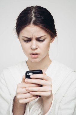 Kadın ellerinde cep telefonuna bakıyor ve beyaz giysi arka planında ışık var.