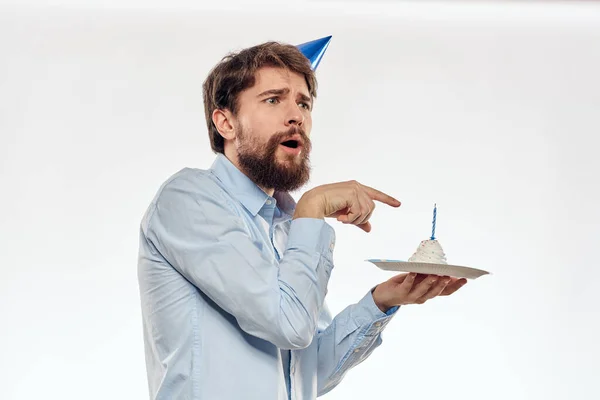 Een man met een baard houdt een taart in zijn hand op een lichte achtergrond verjaardag — Stockfoto