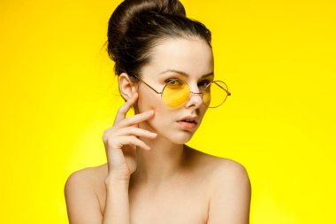 Çıplak omuzlu, sarı gözlüklü bir kadın.