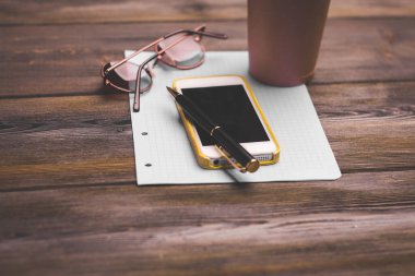 Ofis masası, not defteri gözlükleri, cep telefonu kahve fincanı.