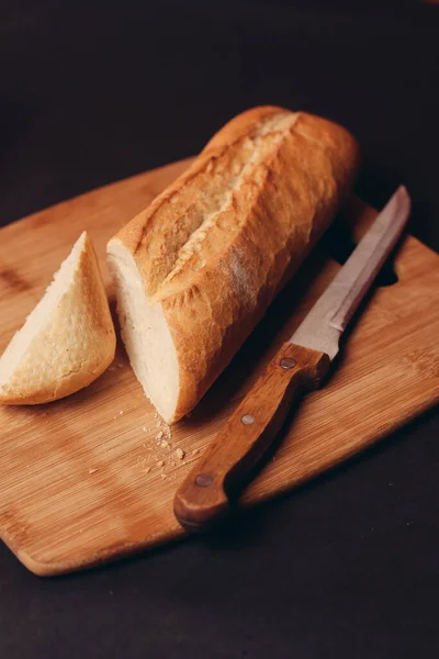 La hogaza del pan cortado sobre la tabla y la cocción los productos horneados el fondo oscuro — Foto de Stock