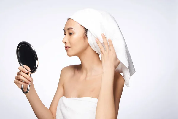 Glad vacker kvinna ser sig i spegeln och en handduk på huvudet hudvård spa behandlingar ljus bakgrund — Stockfoto