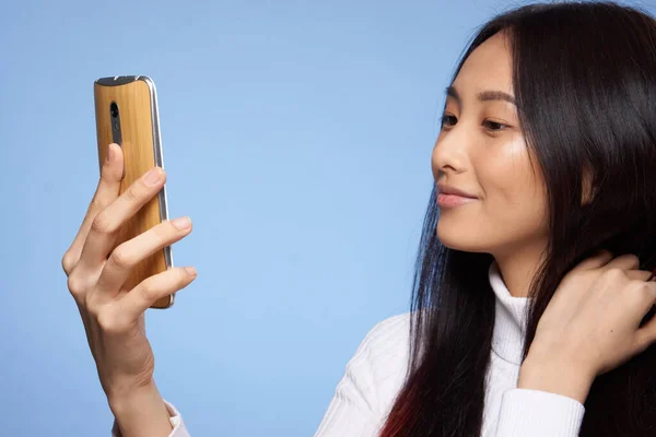 Woman of asian appearance with a phone in her hands blue background — Stock Photo, Image