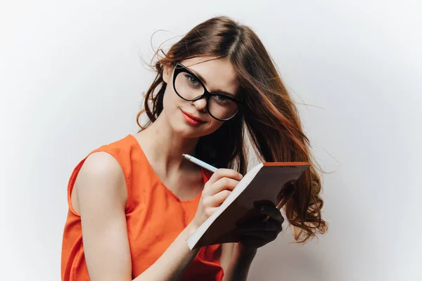 Femme dans une robe de soleil orange sur un fond clair avec un carnet et un stylo à la main un étudiant en éducation — Photo