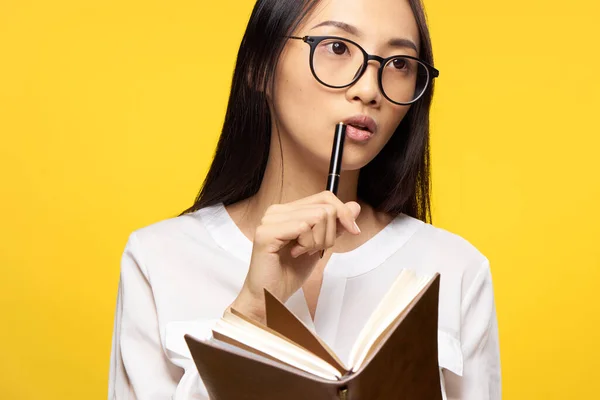 Zakelijke vrouw met een notebook in haar handen houdt een pen in de buurt van haar lippen elegante stijl gele achtergrond — Stockfoto