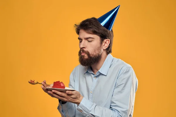 Un hombre con un pastel de cumpleaños en sus manos y con una gorra sobre un fondo amarillo en su cumpleaños — Foto de Stock