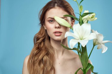 Mavi arka planda beyaz çiçeklerle dolu bir buketi olan çıplak omuzları olan güzel bir kadın.