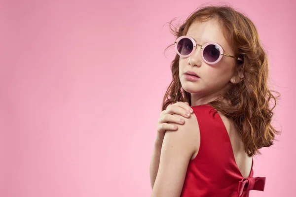 Joyeux petite fille enfance lunettes sombres robe rouge style de vie fond rose — Photo