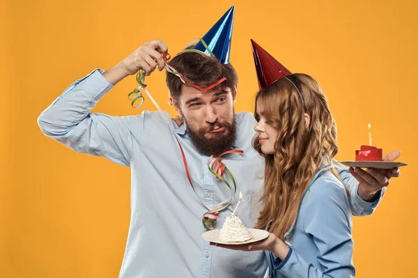 Hombre y mujer en una fiesta en gorras y con pastel de oropel divertido fondo amarillo — Foto de Stock