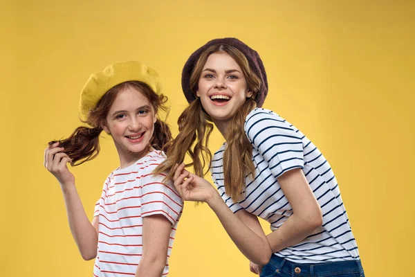 Engraçado mãe e filha vestindo chapéus moda diversão alegria família amarelo fundo — Fotografia de Stock
