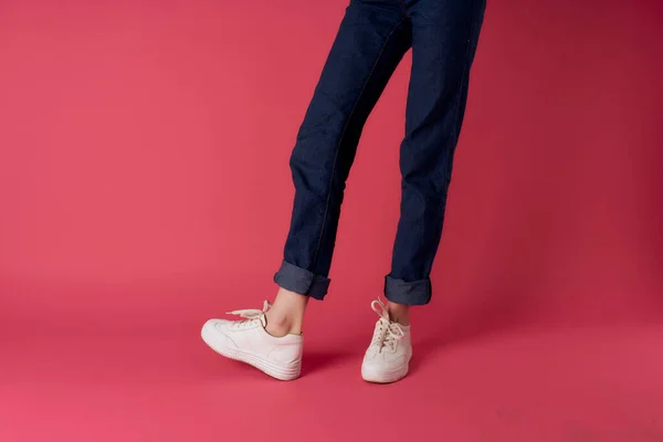 Donna gambe jeans bianco sneakers strada moda studio rosa sfondo — Foto Stock