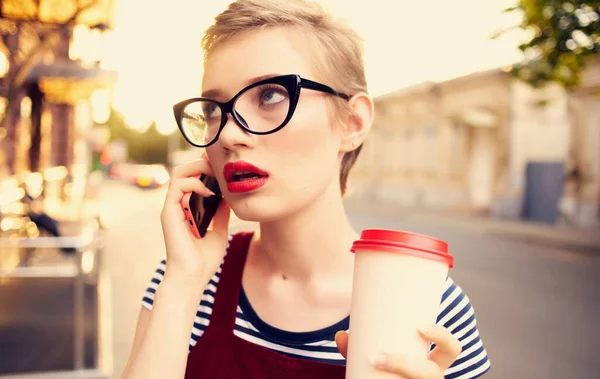 Woman with short hair talking on the phone in the street and a cup of coffee in her hand — Stock Photo, Image