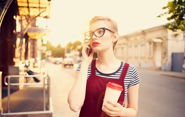 Mujer con el pelo corto hablando por teléfono en la calle y una taza de café en la mano — Foto de Stock