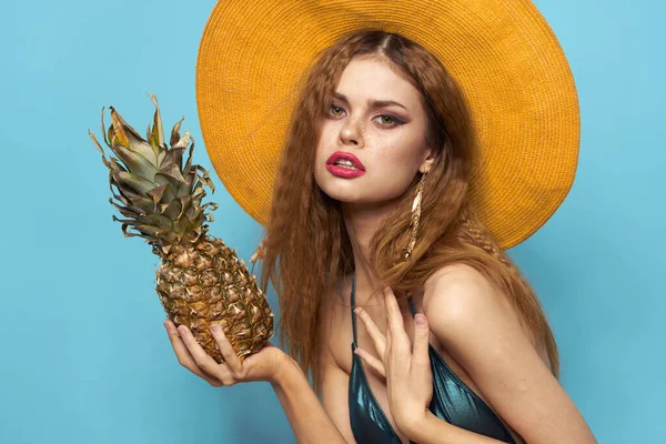 头戴沙滩帽、头戴菠萝、身穿泳衣、身穿异国情调水果蓝色背景休假日的女人 — 图库照片