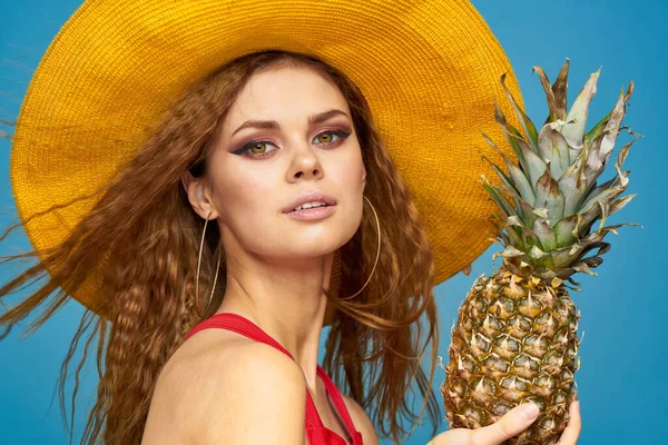 Kvinna i gul hatt med ananas händer lockigt hår exotiska frukter blå bakgrund attraktiv look — Stockfoto