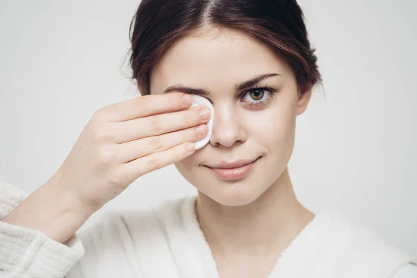 Vrouw in een badjas veegt haar gezicht met een witte spons uiterlijk zorg cosmetologie — Stockfoto
